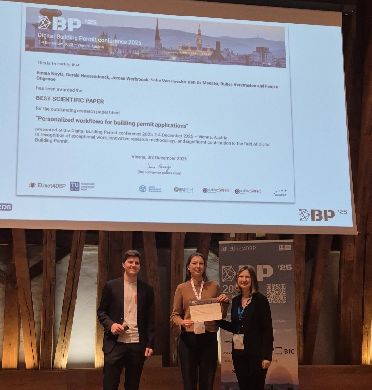 Emma is holding the award while standing on stage, with two other people, in front of a screen mentioning the paper and the award.