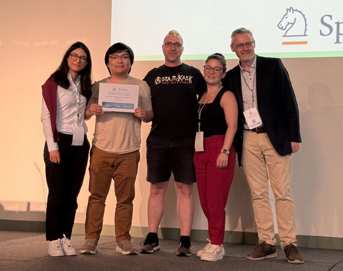 5 people are facing the camera including Sitt Min Oo (2nd person from the left) and Olaf Hartig (person in the middle). Min Oo is holding the Best Research Paper Award.