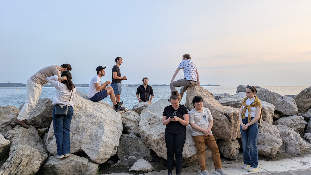 Group picture of 9 people standing on, leaning against, and sittings on big rocks near the sea. The people include Wout, Maarten, Beatriz, Min Oo, and Ruben D.